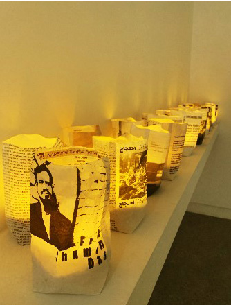A row of small black and white paper packets, lit up with a warm light from the inside. The packet at the forefront of the image depicts a print of a man with writing alongside.
